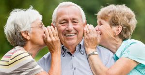 Two older women whispering to a senior man