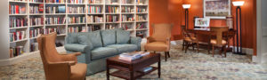 Brightly lit library with a wall of books and comfortable sofa and wing chairs