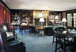 Elegant library with dark leather chairs and sofas, bookshelves set into the walls, and French doors to the hallway