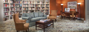 Comfortable sofa and chairs in front of a wall of books in a senior living community library